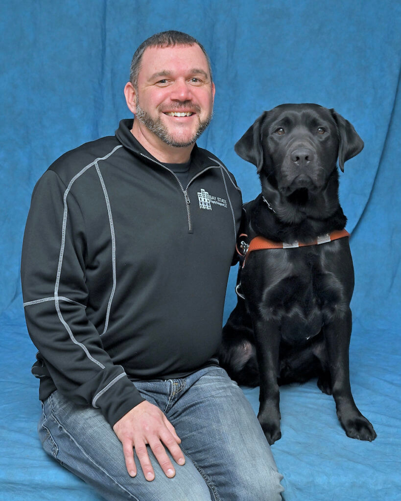 Kevin and black Lab guide dog Jason sit for their team portrait