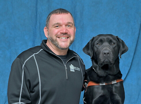 Kevin and black Lab guide dog Jason sit for their team portrait