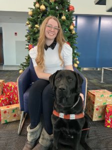 Michaela sits by a Christmas tree with black Lab guide Eleanor