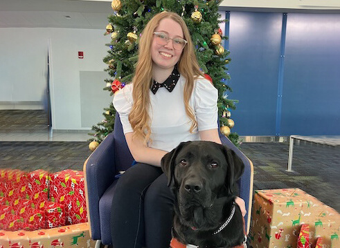 Michaela sits by a Christmas tree with black Lab guide Eleanor