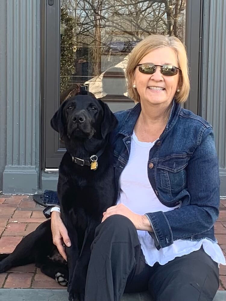 Black Lab pup Miles sits on a step with raiser Sharon