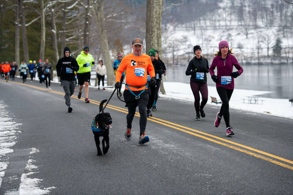 Runner in orange Guiding Eyes sweatshirt runs with Pup