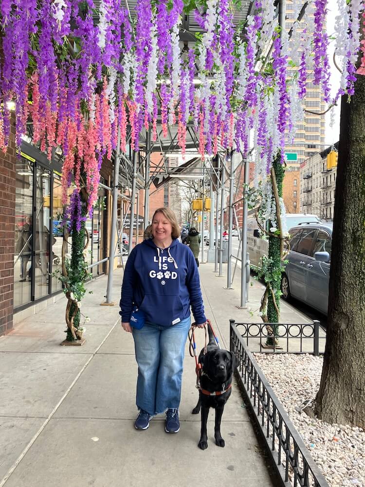 Caitlin wearing Life is Good sweatshirt and Gemini walk under hanging silk flowers in NYC