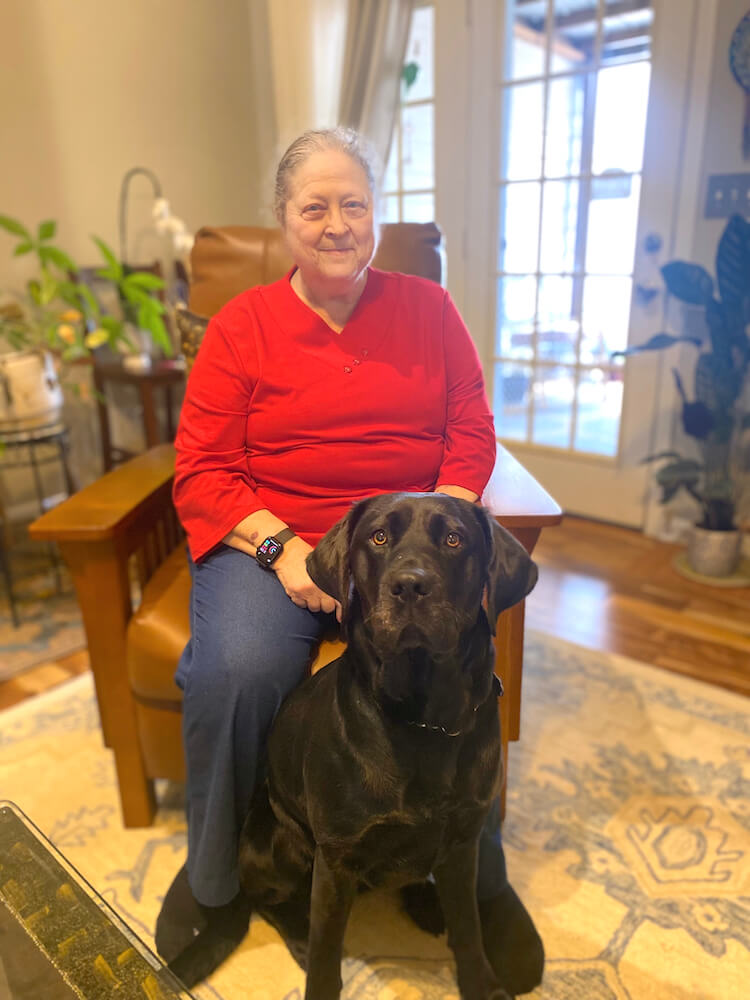 Dory and black Lab guide Fallon in team portrait in room with plants