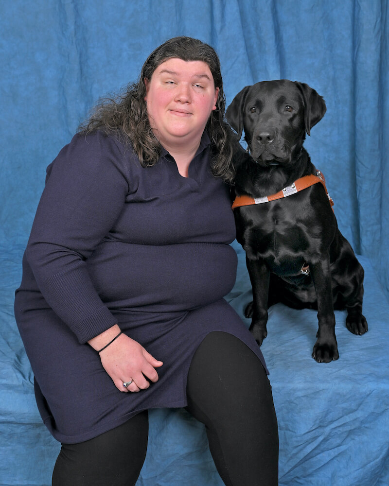 Jennifer and black Lab guide dog Nyssa sit side by side in team portrait