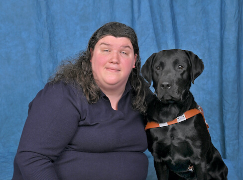 Jennifer and black Lab guide dog Nyssa sit side by side in team portrait