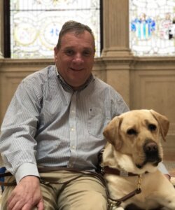 Carl and yellow Lab Tigger sit for team portrait against back drop of stained glass windows