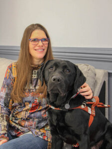 Chantal sits with a hand on the neck of black lab Yoda as they pose for team portrait