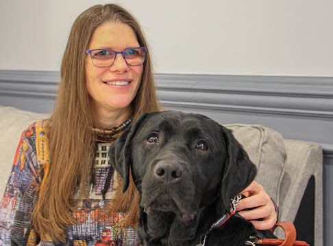 Chantal sits with a hand on the neck of black lab Yoda as they pose for team portrait