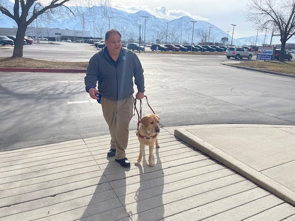 Darran and Merlin walk safely at a Utah shopping center with rocky snowy mountains in the background