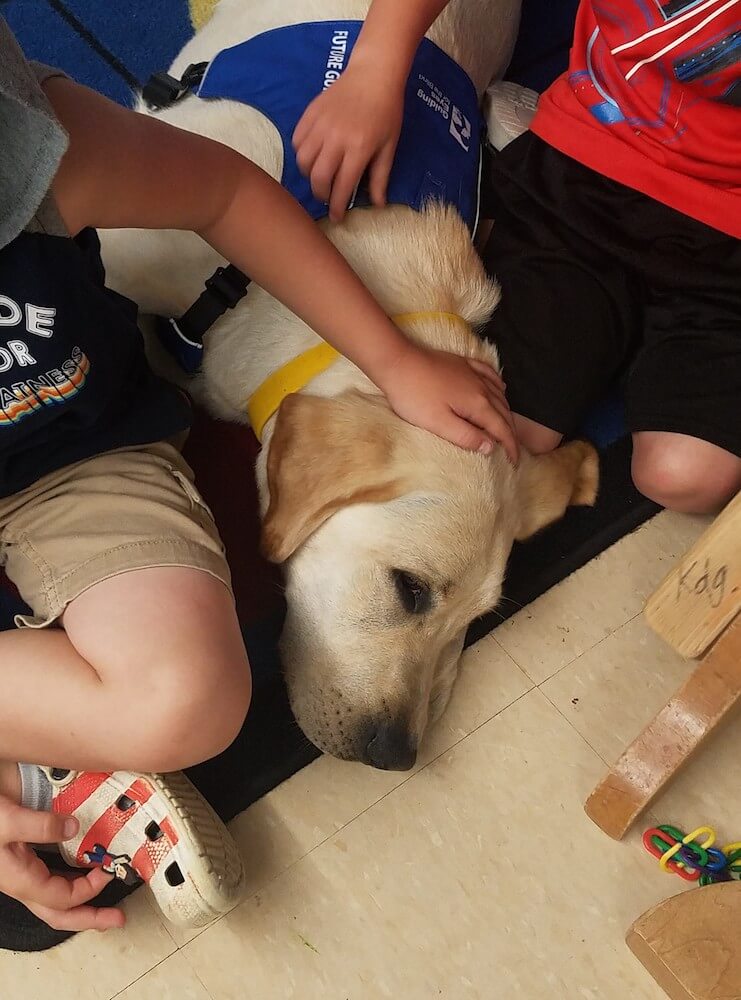 Pup Tigger is gently pet by 1st graders that surround him