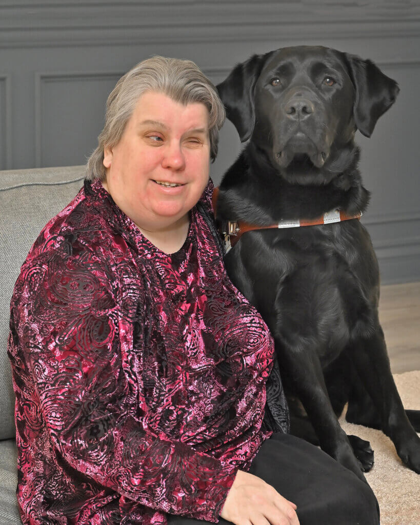 Lisa and black Lab guide Fay sit head to head from their team portrait