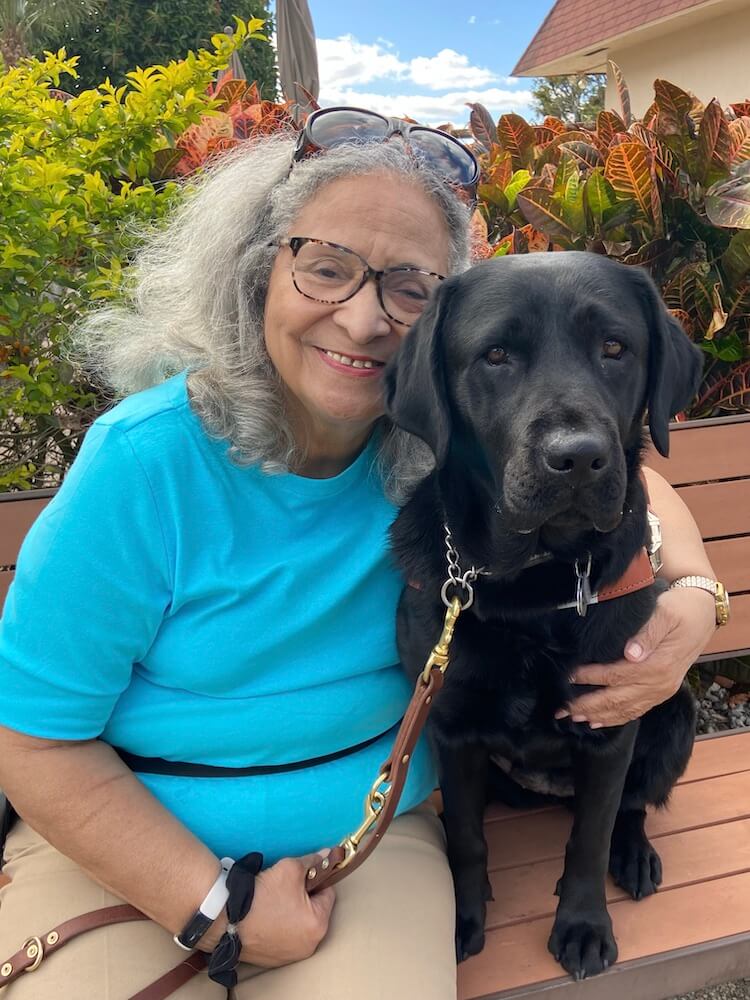 Patricia and black guide dog Eva sit head to head for team portrait