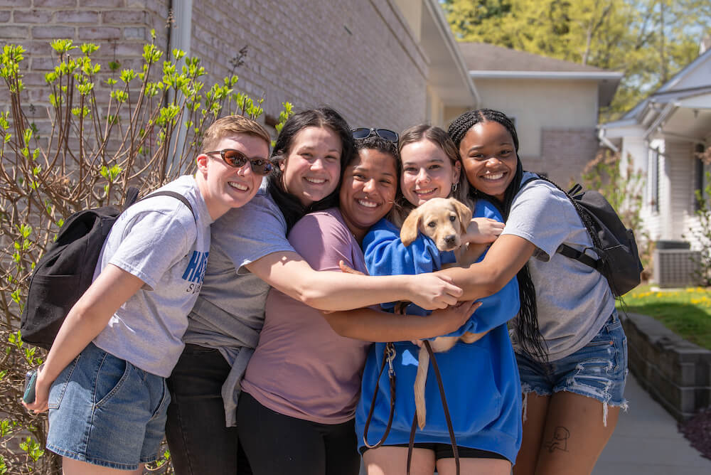 five young women cuddle a small yellow puppy