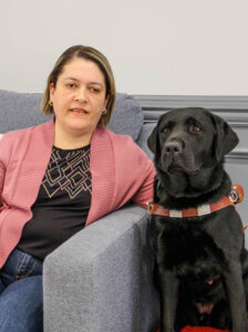 Vivian sits next to black lab guide dog Emmylou for team portrait 