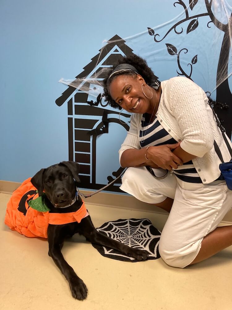 Black Lab Charlene wears a pumpkin costume with raiser Wendy