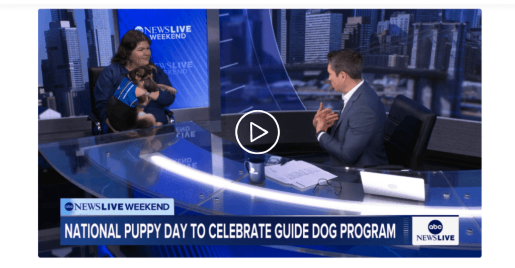 Alissa holds puppy Quartz at the left end of the news desk as the host speaks from the center