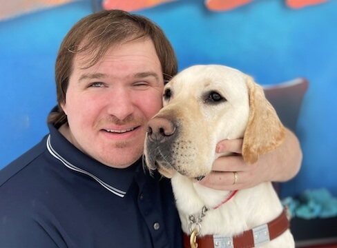 Tony holds yellow Lab guide dog Norris' head close to his with arms around him