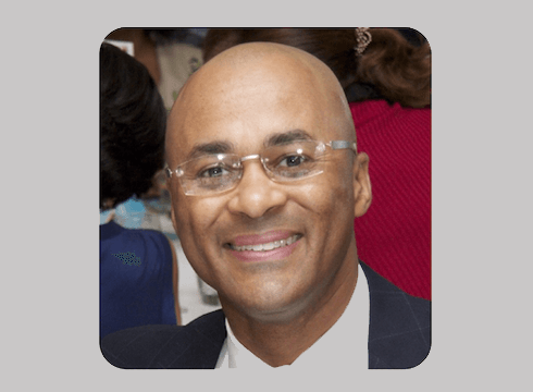 Christopher Perry - new president and CEO -smiles in a headshot photo. He is wearing rimless glasses and a dark suit with a white shirt.