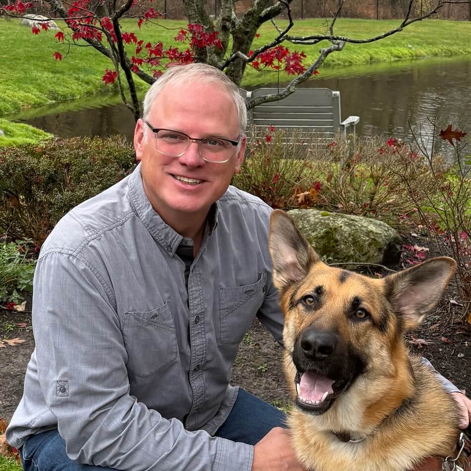 Gerald Brenninkmeyer Director of Training with a German Shepherd in harness in front of a pond, plantings and a large decorative rock