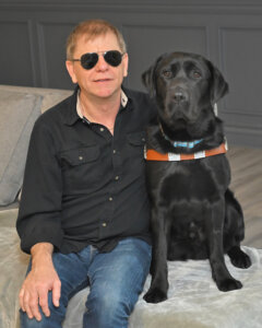 Jeff sits with black Lab guide dog Guthrie for team portrait