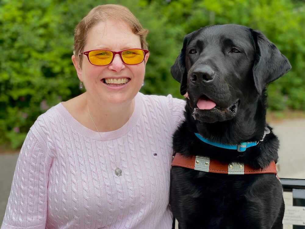Karen and black lab guide Bart sit outside for their team portrait
