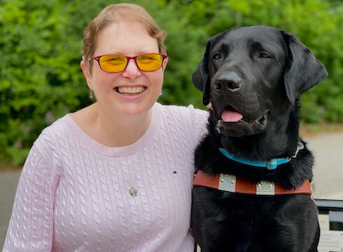 Karen and black lab guide Bart sit outside for their team portrait