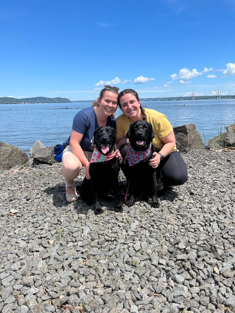 Liberty sits with raisers and a black Lab on a rocky shore