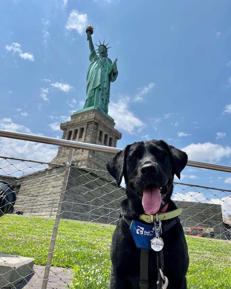 Liberty poses with blue skies & the Statue of Liberty behind her