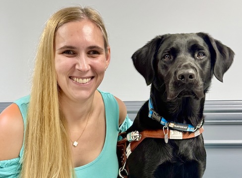 Mikayla and black lab guide dog Tally are sitting for their graduate team portrait