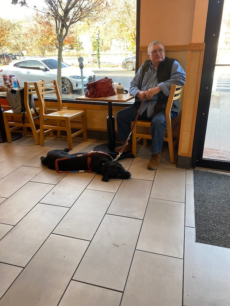Rene sits in a coffee shop while guide Yonder patiently rests on the floor
