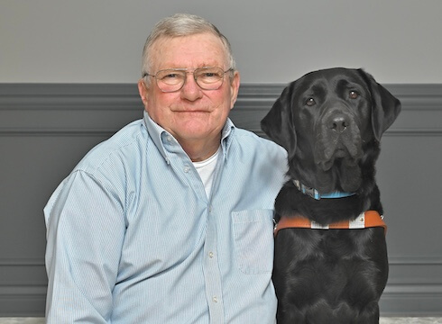 Rene sits with black Lab guide dog Yonder for their team portrait