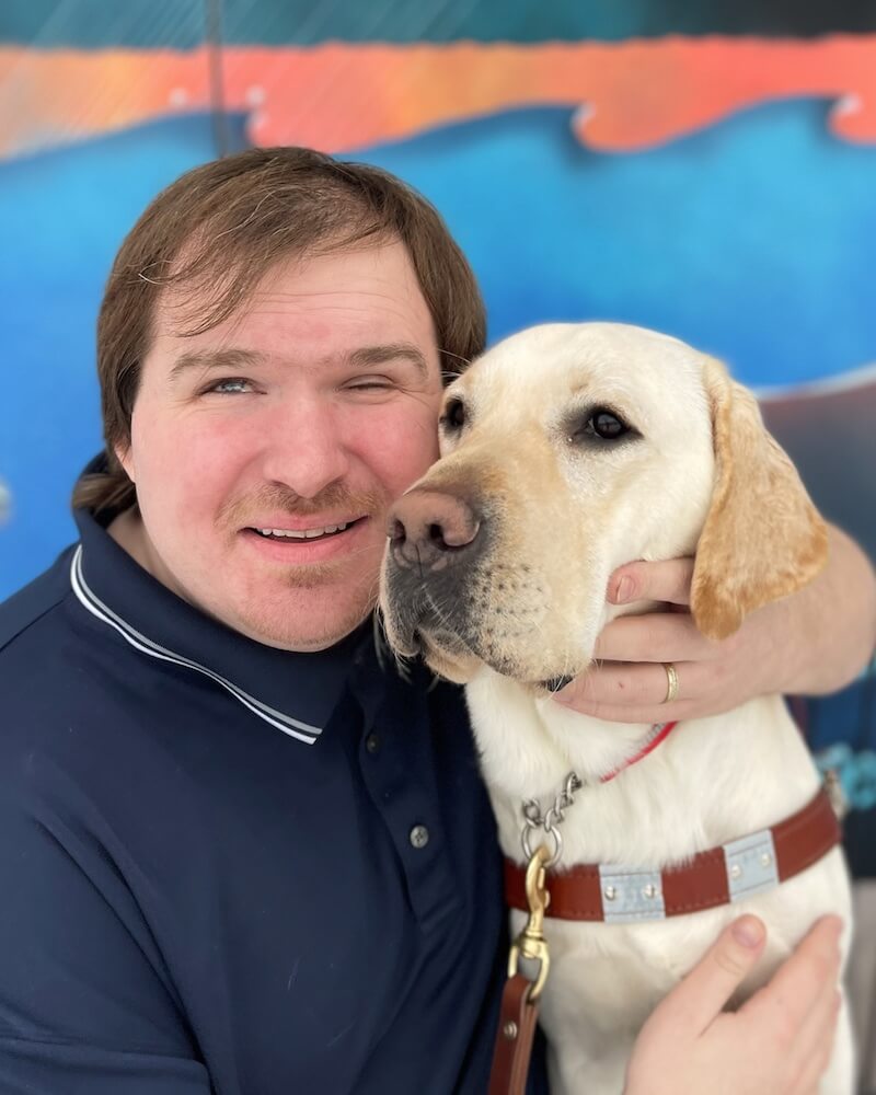 Tony holds yellow Lab guide dog Norris' head close to his with arms around him