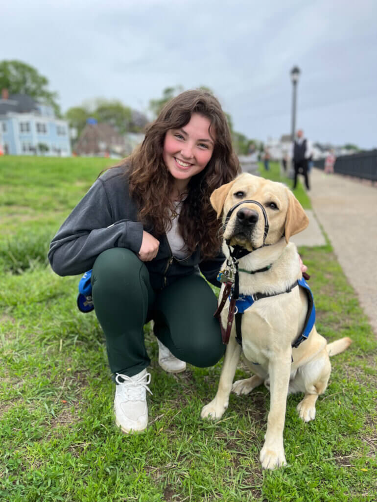 Yellow Lab pup on program Justice with kneeling raiser beside him