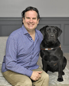 Christian and black lab guide dog Gideo sit close indoors for grad portrait