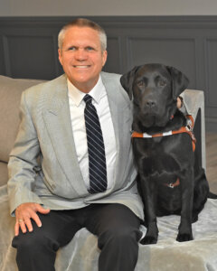Joe and black lab guide dog Martha sit indoors for team portrait