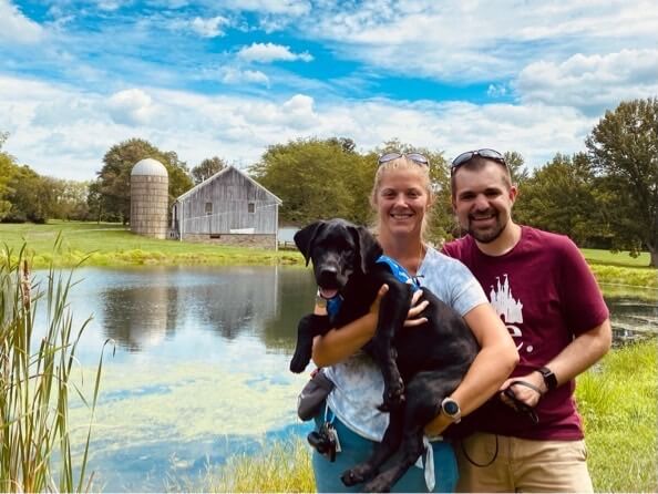 raisers hold pup Kenneth against backdrop of pond, barn and silo