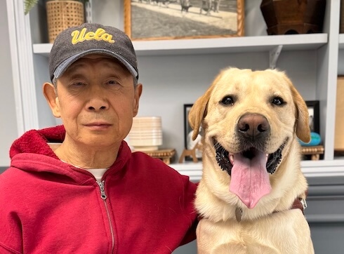 Mark and yellow Lab guide dog Justice sit in front of shelves filled with various items for their team portrait