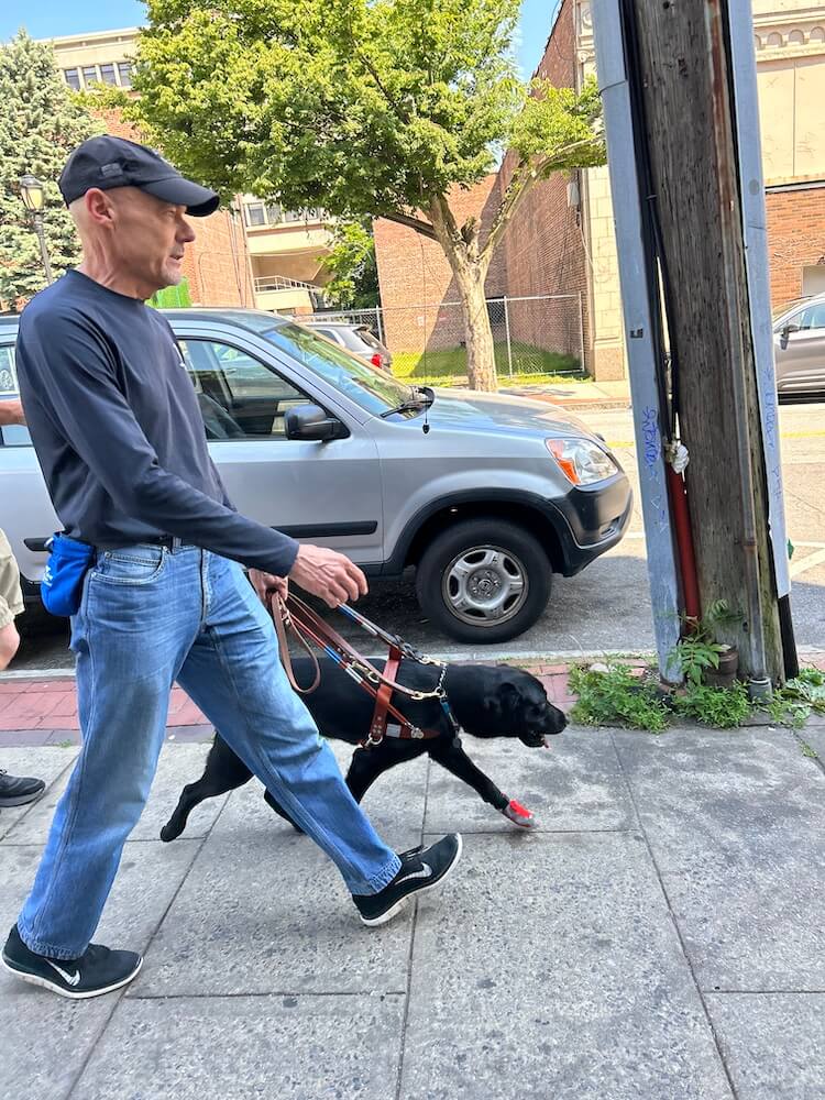 Tony and Imari walk quickly down a sidewalk with the street and utility pole to their left