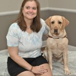 Ashley and yellow Lab guide Hawaii sit for team portrait