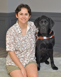 Sofia sits with black lab guide dog Winsome for their team photo