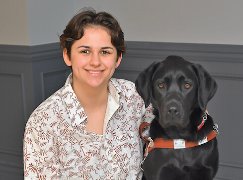 Sofia sits with black lab guide dog Winsome for their team photo