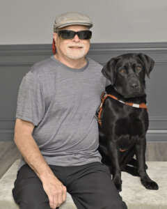 James sits next to black lab guide dog Peony for their formal guide dog portrait