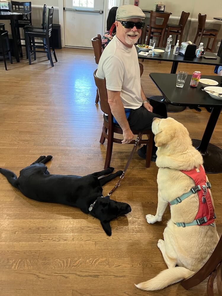 James sits at the table in Rosie's Cafe on campus with Peony stretched out below