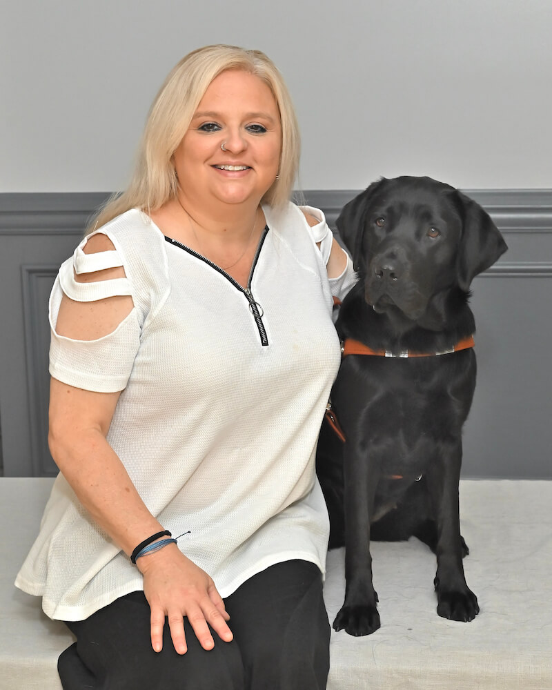 Mandy and black lab guide dog Reina sit for graduate portrait
