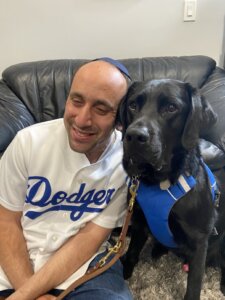 Menachem in a Dodgers shirt leans in towards black Lab guide dog Sumatra