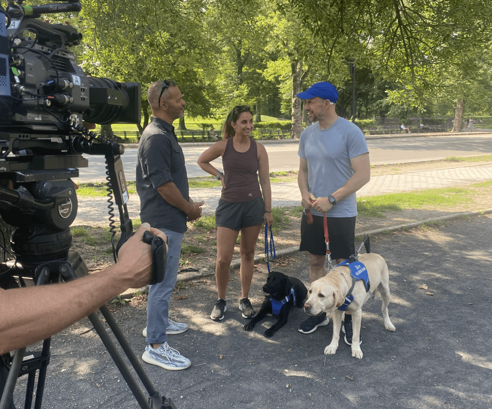Interviewer David stands in the park with Peyden, Thomas and two guide dogs