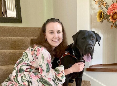 Rachel and black lab guide dog Chris sit for their team portrait on indoor steps
