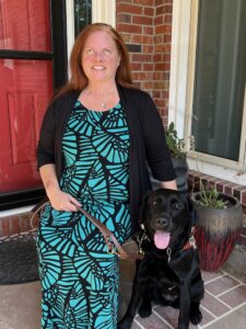 Amy sits on a porch with black Lab Guide dog Fairlee for their team portrait