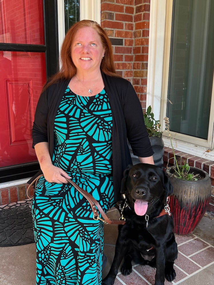 Amy sits on a porch with black Lab Guide dog Fairlee for their team portrait